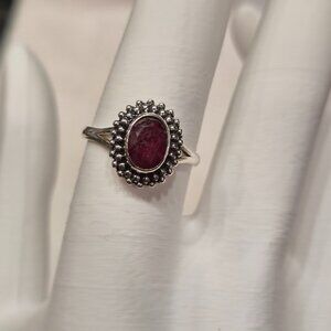 Sterling silver ring with an oval-shaped ruby gemstone in a beaded halo setting